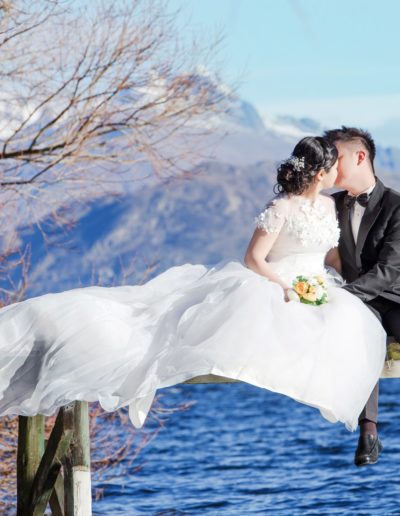 Bride and Groom Sitting on Pier over lake in picturesque setting
